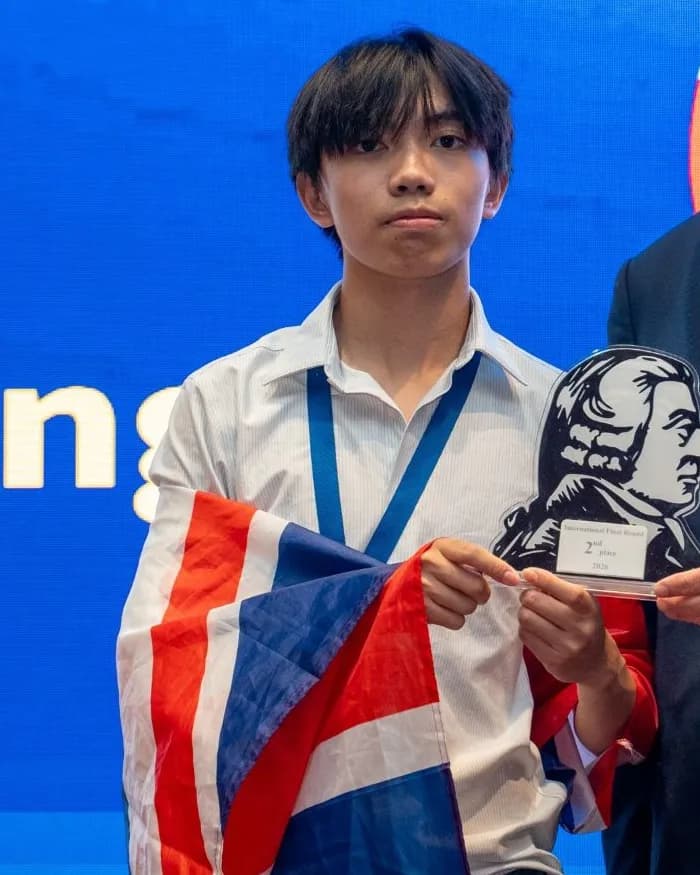 The founder holding the 2nd place trophy and a flag at the 2026 International Final
